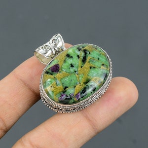 May include: Oval-shaped pendant with a green, gold, and pink gemstone set in silver. The pendant has a detailed silver bail.