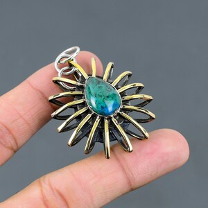 May include: A silver and gold pendant with a green gemstone in the center. The pendant is shaped like a sun with rays extending out from the center.