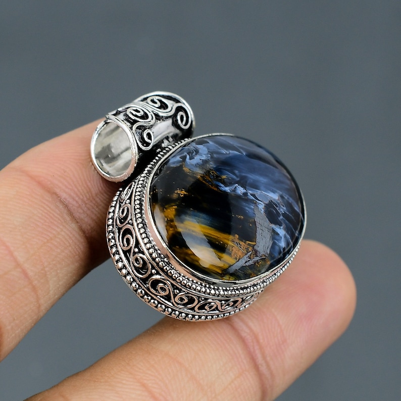 May include: Silver pendant with a blue and gold tiger's eye gemstone. The pendant has an ornate silver design around the gemstone.