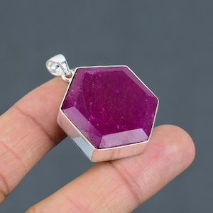 Może przedstawiać: Wisiorek w kształcie sześciokąta z rubinem osadzonym w srebrze próby 925. Rubin jest intensywnie czerwony i ma szlif fasetkowy. Wisiorek ma średnicę około 2,5 cm.