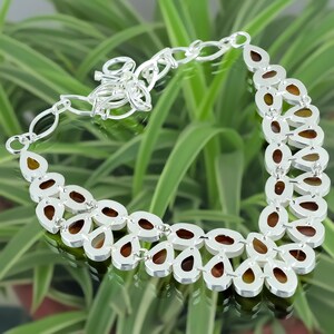 May include: A silver necklace with a teardrop-shaped design. The necklace is made of silver and has a brown stone in the center of each teardrop. The necklace is on a green background.