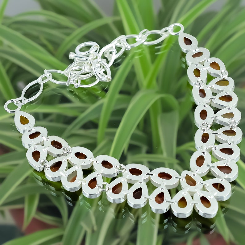 May include: A silver necklace with a teardrop-shaped design. The necklace is made of silver and has a brown stone in the center of each teardrop. The necklace is on a green background.