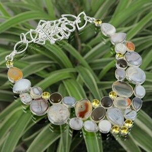 May include: A silver necklace with a clasp closure features a variety of agate stones in shades of gray, white, and brown, with yellow citrine accents.