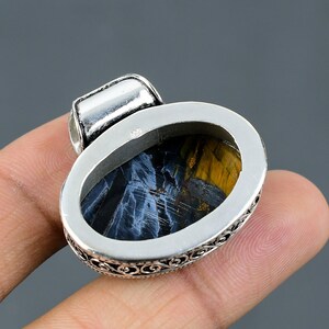 May include: Silver pendant with an oval-shaped blue and gold tiger's eye gemstone. The pendant has an intricate silver border.