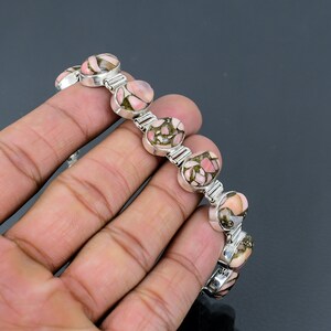 May include: A silver bracelet with pink and green oval-shaped stones. The bracelet is made of a chain with small silver links.