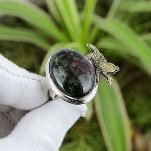 Puede incluir: Un anillo de plata con una piedra preciosa verde y rosa y un diseño de animal dorado.