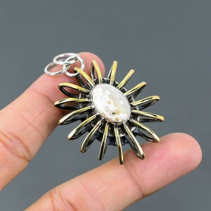 May include: A silver and gold pendant in the shape of a sun with a white agate stone in the center.
