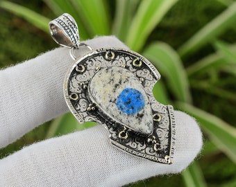 Könnte beinhalten: Ein silberner Anhänger mit einem komplizierten Design, das einen blauen und weißen Edelstein zeigt. Der Anhänger ist herzförmig und hat einen detaillierten, verzierten Rand.