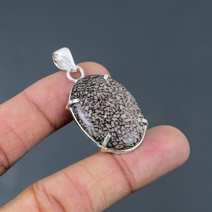 May include: A silver pendant featuring a fossilized dinosaur bone oval cabochon with a detailed pattern. The pendant is set in a silver bezel with a bail for attaching a chain.