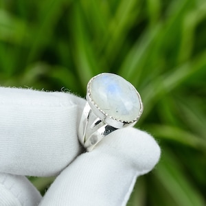 May include: A silver ring with a white oval moonstone set in a silver bezel. The ring has a delicate, open band.