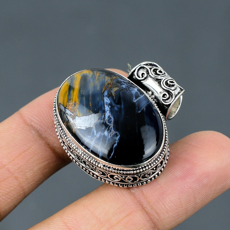 May include: A silver pendant with an oval blue and gold tiger's eye gemstone. The pendant has an ornate silver frame with a decorative bail.