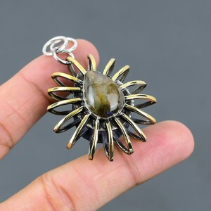 May include: A silver and gold pendant featuring a teardrop-shaped labradorite gemstone set in a sunburst design.