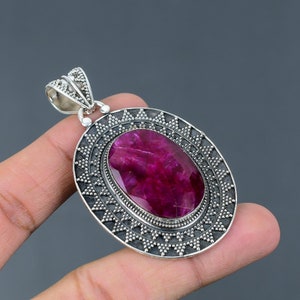 May include: A silver pendant with a large, oval-shaped, pink ruby gemstone set in a silver frame with a decorative, geometric design.