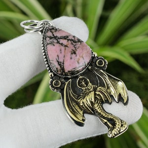 Op de afbeelding: Een zilveren hanger met een roze en zwarte edelsteen en een gouden drakenontwerp.