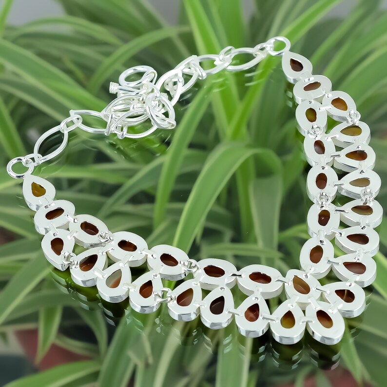 May include: A silver necklace with a teardrop-shaped design. The necklace is made of silver and has a brown stone in the center of each teardrop. The necklace is on a green background.