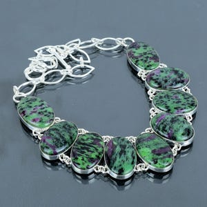 May include: A silver necklace with a chain and oval-shaped green and pink gemstones.