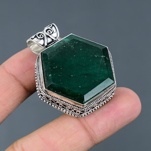 Pode incluir: Um pingente de prata com uma grande gema verde facetada engastada em uma moldura hexagonal. O pingente tem um design filigrana intrincado em torno da gema.