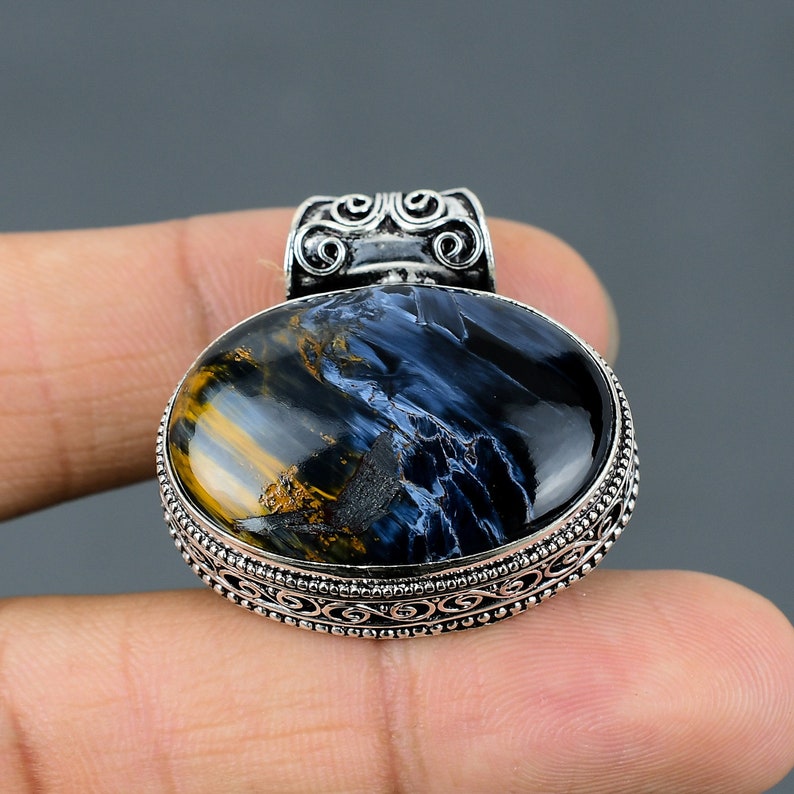 May include: A silver pendant with a blue and gold tiger's eye gemstone. The pendant has an ornate silver frame with a detailed design.