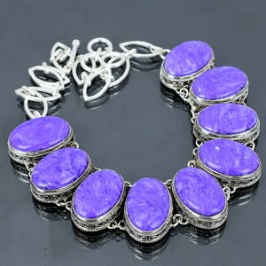 Puede incluir: Un collar de plata con una cadena y siete piedras ovaladas de color púrpura. Las piedras están engastadas en plata y tienen un patrón de mármol.