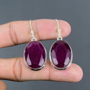 May include: A pair of sterling silver earrings with oval-shaped ruby gemstones. The earrings have a simple design and are perfect for everyday wear.