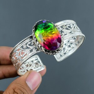 Può includere: Un braccialetto in argento con una chiusura circolare e una pietra preziosa ovale di colore arcobaleno incastonata in una ghiera d'argento. Il braccialetto ha un delicato design floreale.