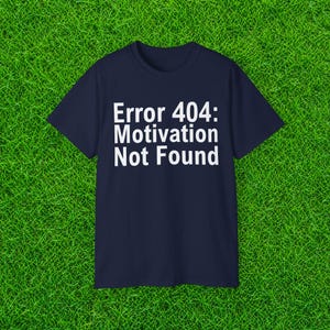 May include: A dark navy blue short-sleeved t-shirt featuring the white printed text Error 404: Motivation Not Found centered on the chest. The garment has a classic crew neckline and a simple, straight-cut silhouette made of solid fabric.