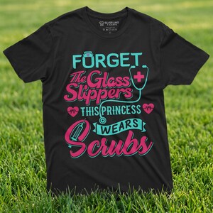 May include: Black t-shirt featuring the text "FORGET The Glass Slippers THIS PRINCESS WEARS Scrubs" in teal and pink. The design includes a stethoscope, a nurse's hat, and a heart symbol.