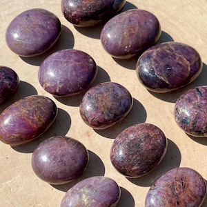 May include: A collection of 14 smooth, polished purple and red ruby tumbled stones. The stones are oval shaped and have a natural, organic look.