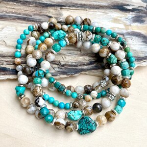 Könnte beinhalten: Ein Set aus sieben Armbändern mit Türkis- und braunen Achatperlen mit silbernen Akzenten. Die Armbänder sind übereinander gelegt und in einem Kreis angeordnet.