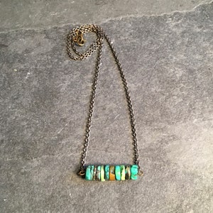 May include: A turquoise and gold necklace with a bar pendant made of stacked turquoise stones. The necklace is on a silver chain.