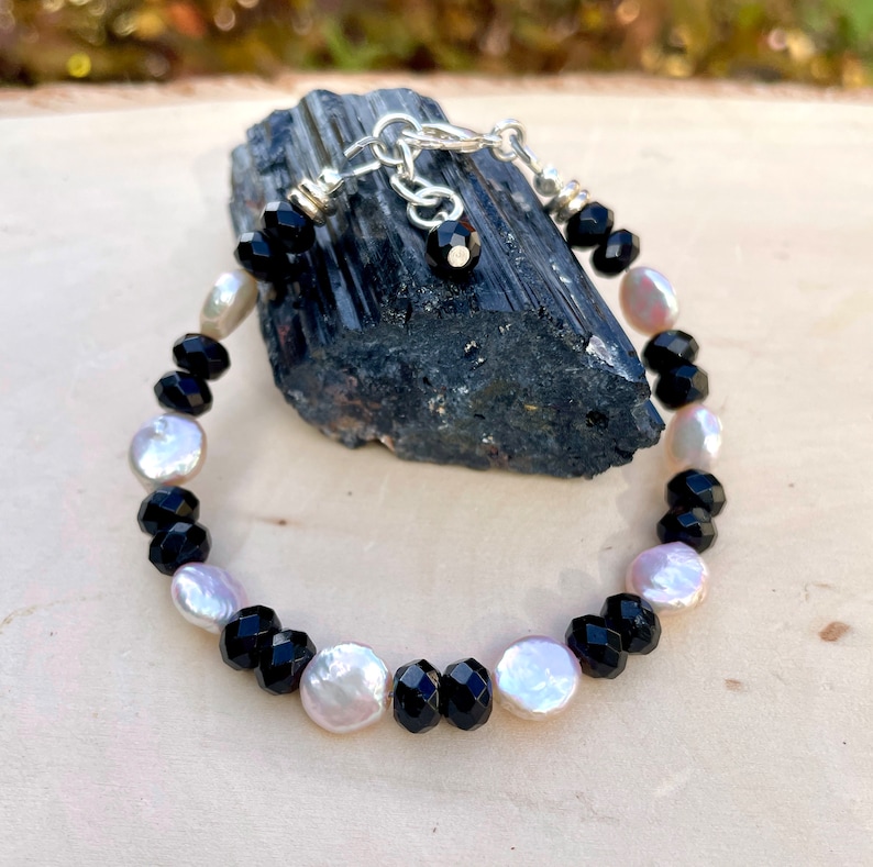 Peut inclure: Un bracelet noir et blanc avec des perles facett&eacute;es noires et des perles blanches nacr&eacute;es. Le bracelet est r&eacute;alis&eacute; avec un fermoir et une cha&icirc;ne en argent.