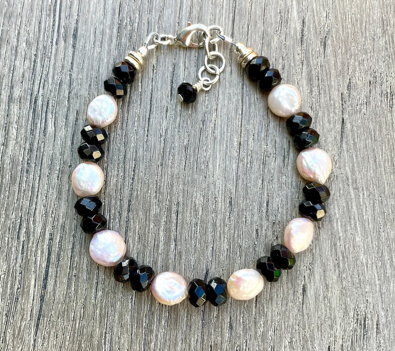 Peut inclure: Un bracelet avec des perles facett&eacute;es noires et des perles blanches altern&eacute;es.