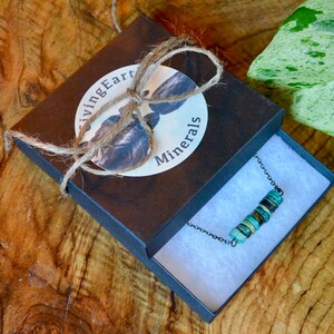 May include: A turquoise and brown beaded necklace in a black box with a white label that says "Living Earth Minerals". The box is tied with twine.