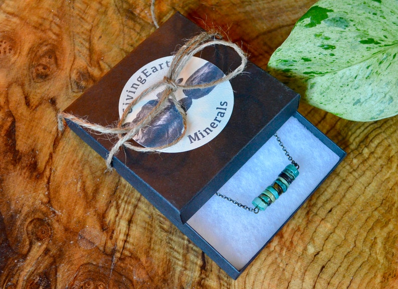May include: A turquoise and brown beaded necklace in a black box with a white label that says "Living Earth Minerals". The box is tied with twine.