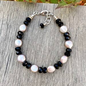 Peut inclure: Un bracelet en perles noires et blanches avec un fermoir argent&eacute;. Le bracelet pr&eacute;sente des perles facett&eacute;es noires et des perles blanches nacr&eacute;es altern&eacute;es.