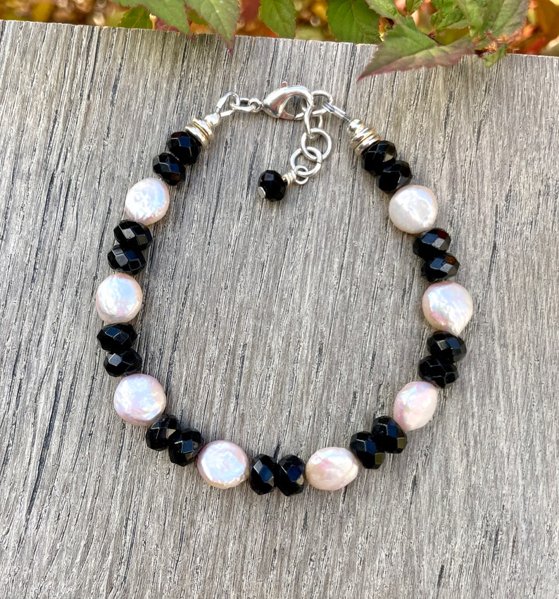 Peut inclure: Un bracelet en perles noires et blanches avec un fermoir argent&eacute;. Le bracelet pr&eacute;sente des perles facett&eacute;es noires et des perles blanches nacr&eacute;es altern&eacute;es.
