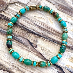 May include: A turquoise beaded bracelet with gold-colored accents. The bracelet features oval and round turquoise beads, interspersed with gold-colored spacers and a rectangular clasp. The beads have variations in color, from light to dark turquoise.