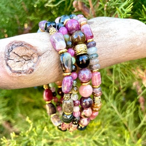 May include: A set of four bracelets featuring a variety of colorful gemstones, including pink, green, and black. The bracelets are made with small, round beads and are strung on elastic cord.