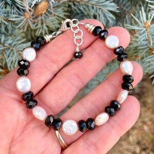 Peut inclure: Un bracelet en perles noires et blanches avec un fermoir argent&eacute;. Le bracelet pr&eacute;sente des perles facett&eacute;es noires et des perles blanches altern&eacute;es.