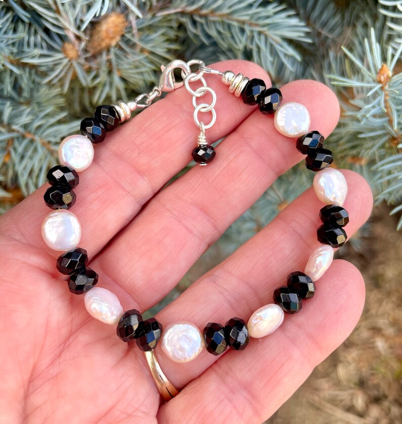 Peut inclure: Un bracelet en perles noires et blanches avec un fermoir argent&eacute;. Le bracelet pr&eacute;sente des perles facett&eacute;es noires et des perles blanches altern&eacute;es.