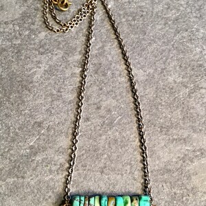 May include: A turquoise and gold necklace with a chain and a bar of turquoise stones.