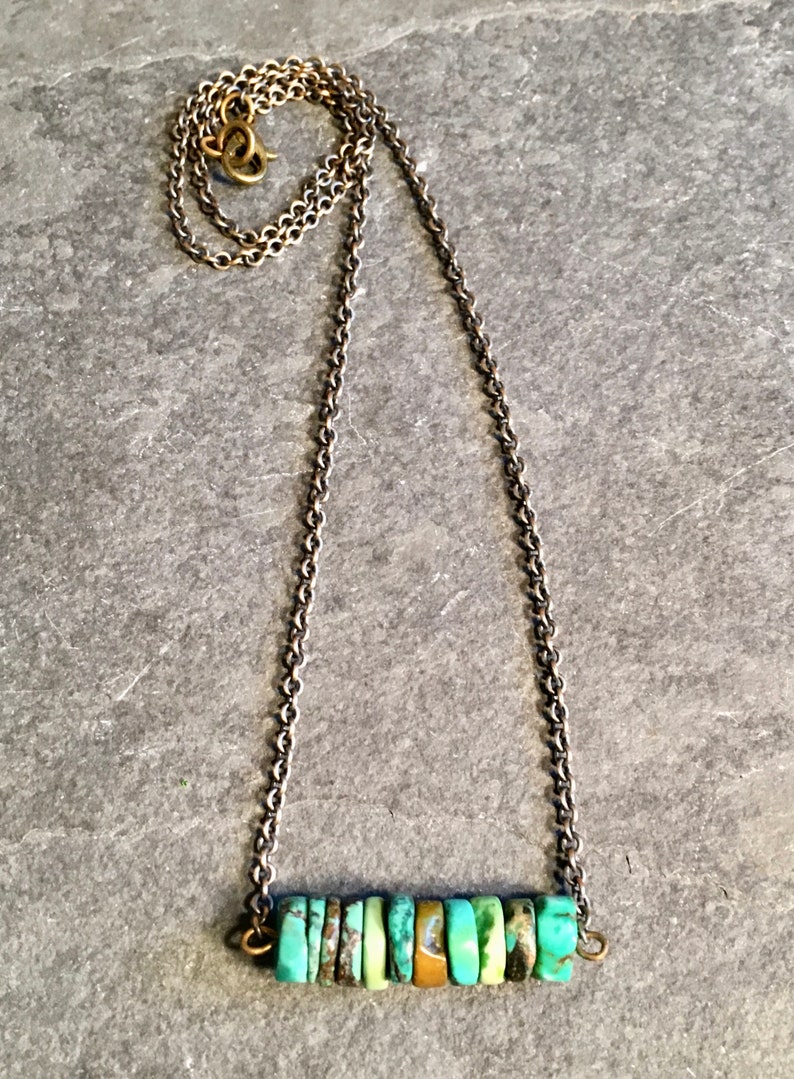 May include: A turquoise and gold necklace with a chain and a bar of turquoise stones.