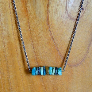 May include: A silver chain necklace with a bar pendant made of turquoise and brown stones.