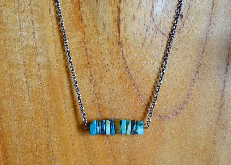 May include: A silver chain necklace with a bar pendant made of turquoise and brown stones.