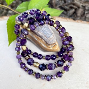 May include: A triple strand bracelet featuring amethyst beads and gold-toned spacers. The bracelet is made with faceted and round amethyst beads.