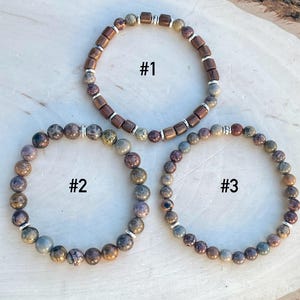 K&ouml;nnte beinhalten: Drei Armb&auml;nder mit braunen und grauen Perlen. Die Armb&auml;nder sind mit 1, 2 und 3 nummeriert.