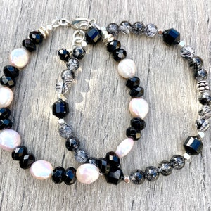 Peut inclure: Deux bracelets avec des perles noires, blanches et grises. Un bracelet a des perles noires et blanches, tandis que l'autre a des perles noires et grises.