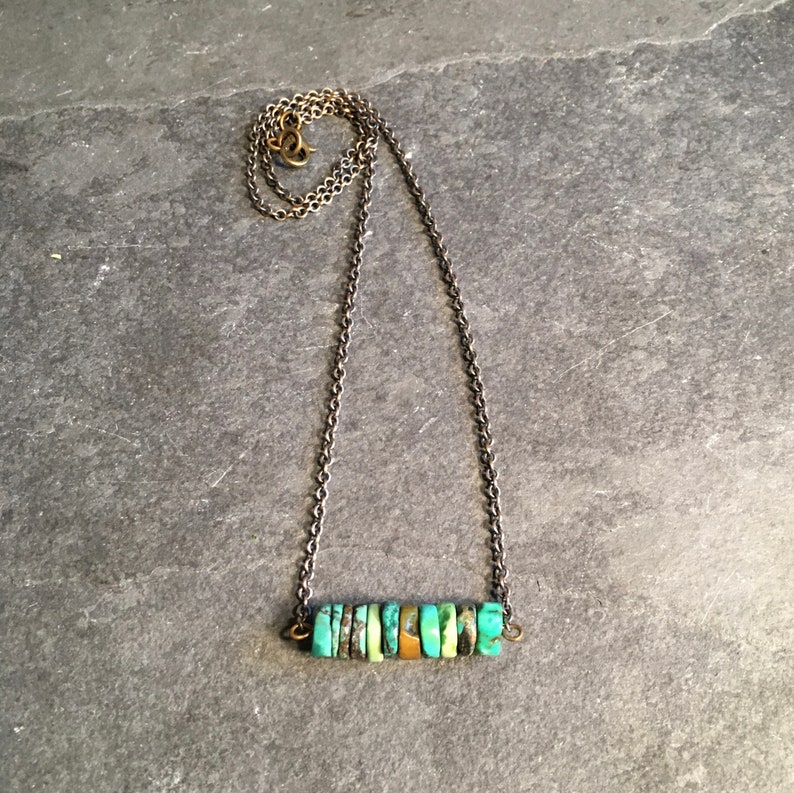 May include: A turquoise and gold necklace with a bar pendant made of stacked turquoise stones. The necklace is on a silver chain.