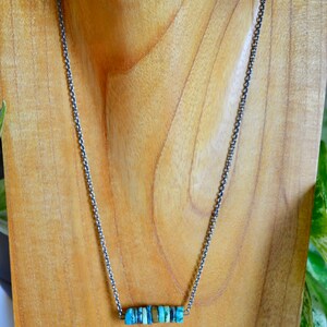 May include: A silver chain necklace with a bar pendant made of turquoise stones.