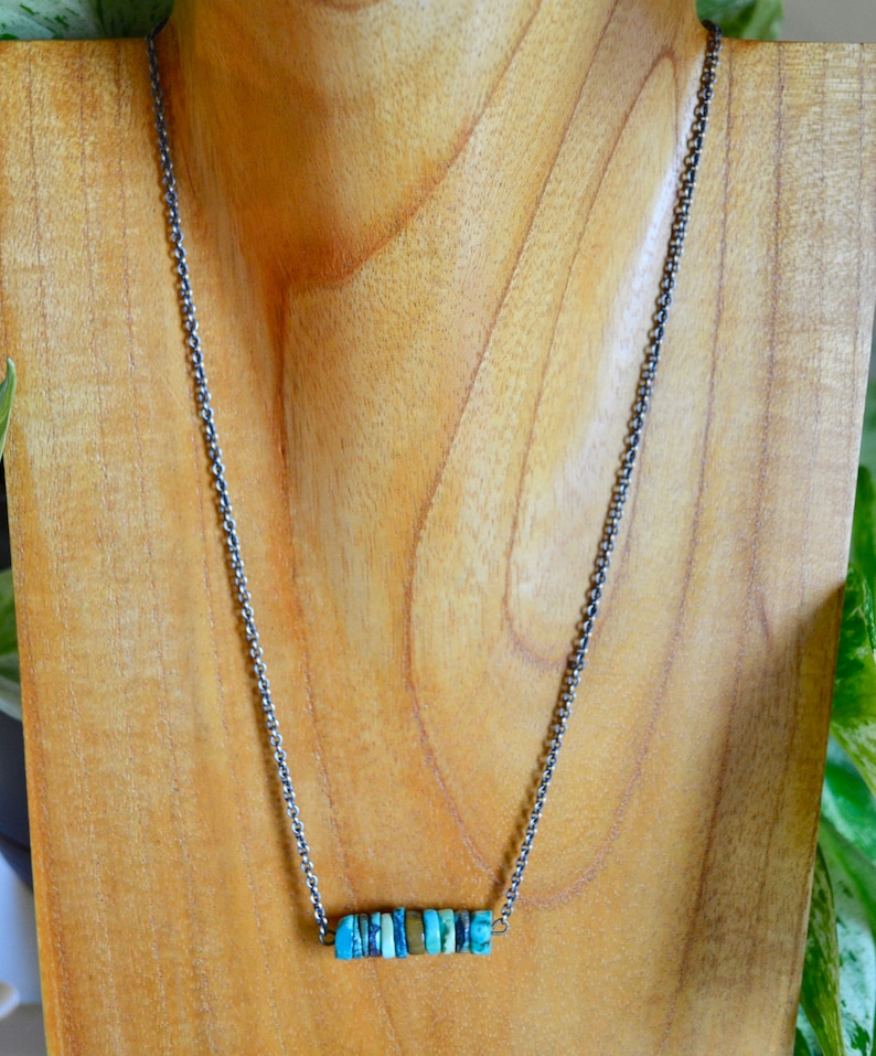 May include: A silver chain necklace with a bar pendant made of turquoise stones.